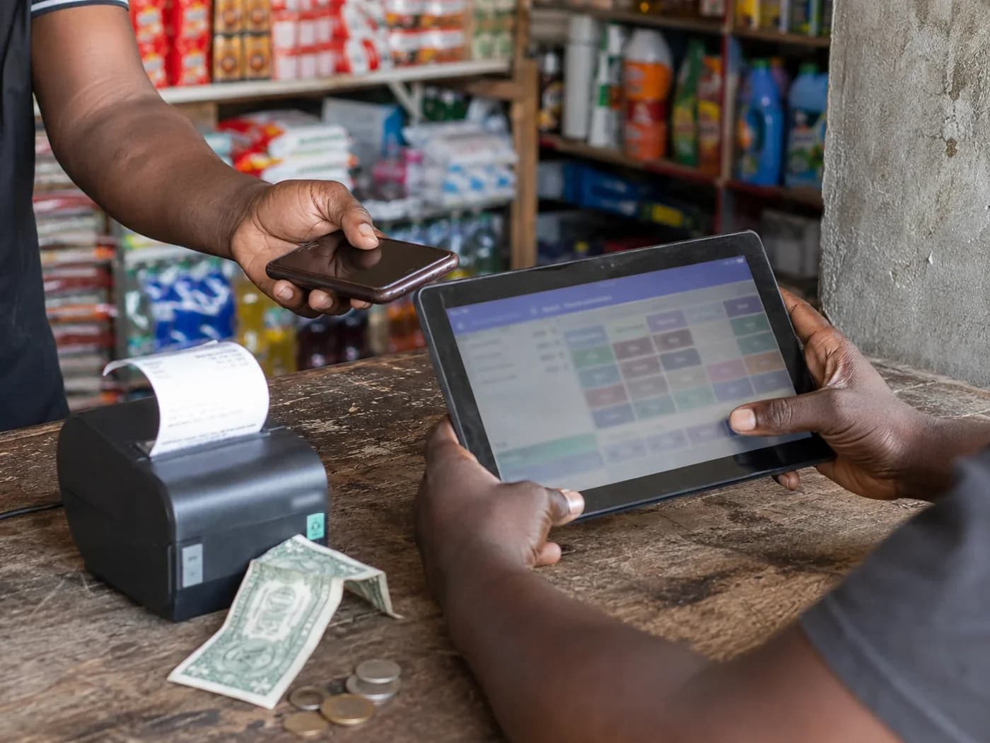 A customer paying at a shop counter while the shopkeeper rings the basket up on a tablet till